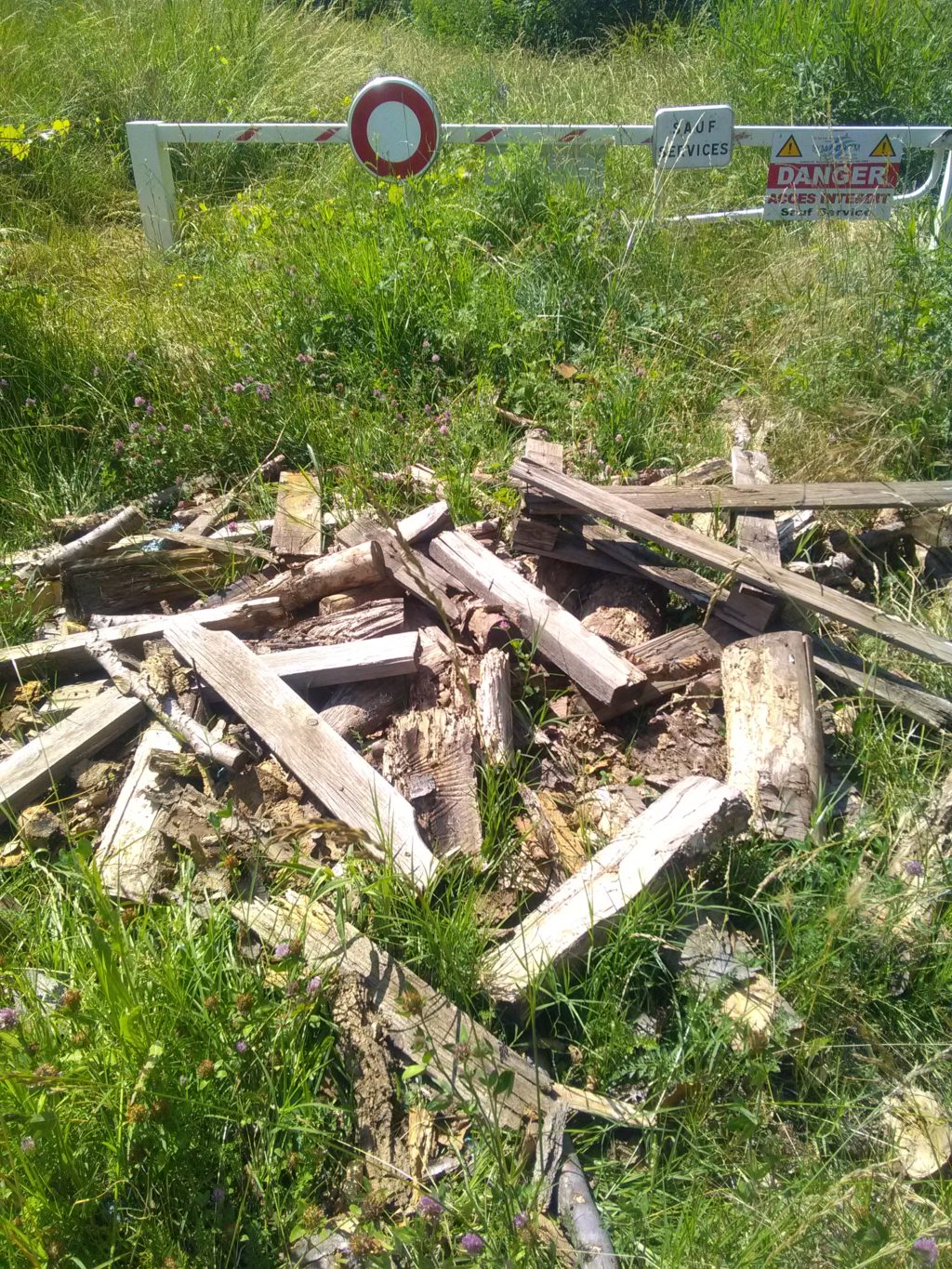 Dépôt sauvage de bois devant une barrière d'accès à la digue